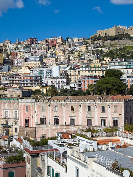 View of Castel Sant'Elmo atop a hill in Naples, Italy, with colorful buildings below.
