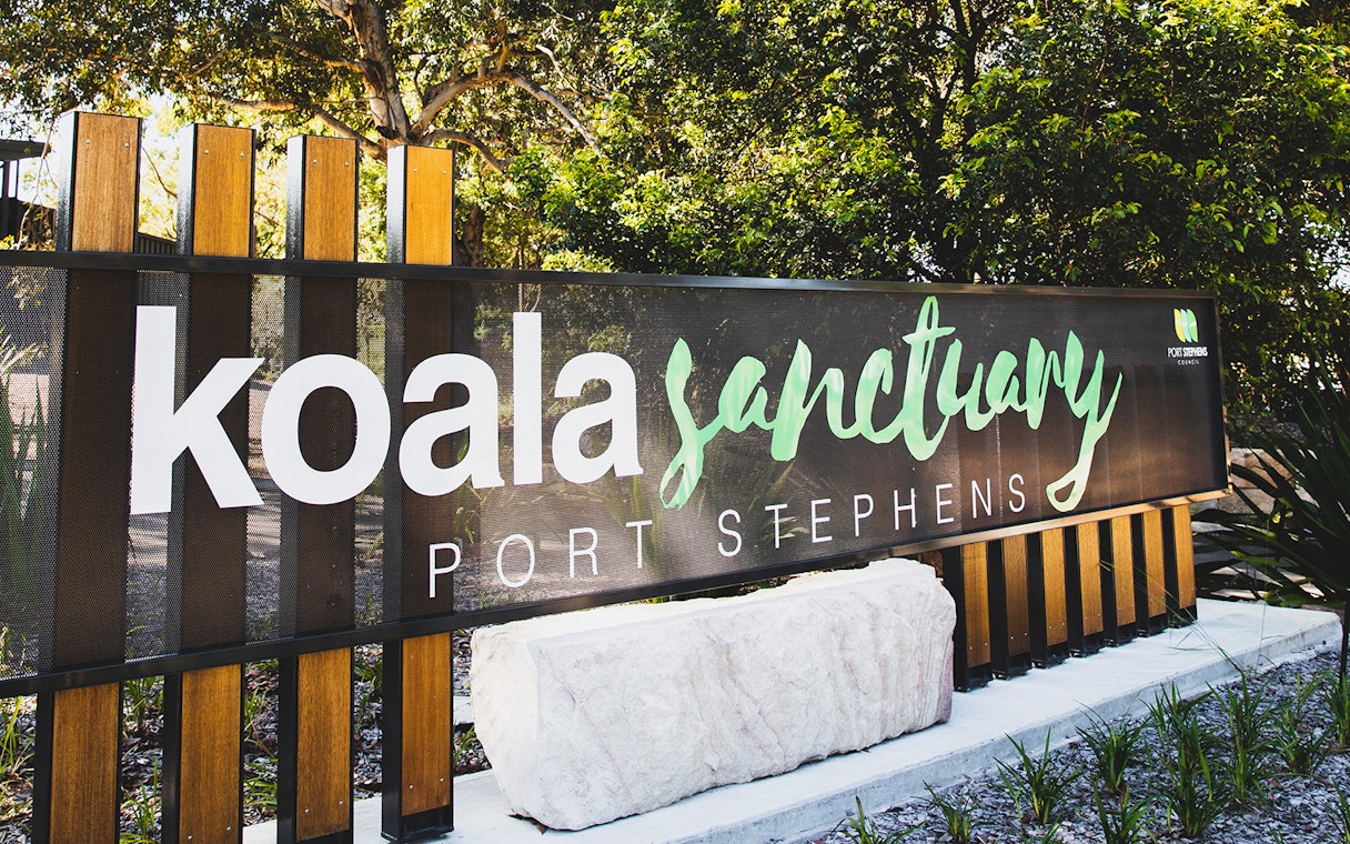 Port Stephens Koala Sanctuary entrance sign surrounded by trees.