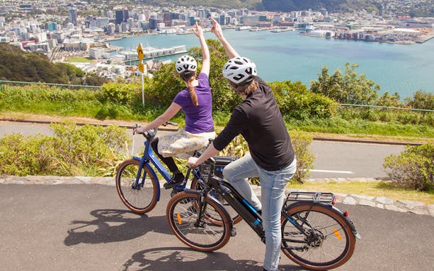Two cyclists on e-bikes overlooking Wellington city and harbor.