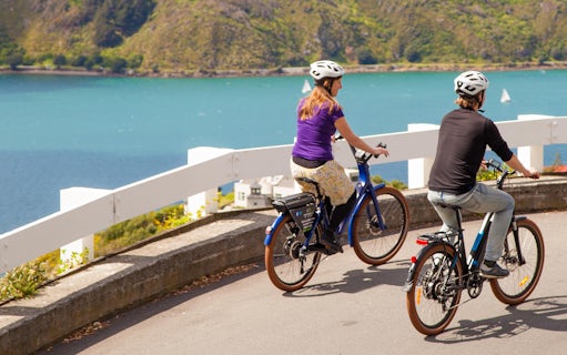 Two people riding e-bikes along a coastal path in Wellington, New Zealand.