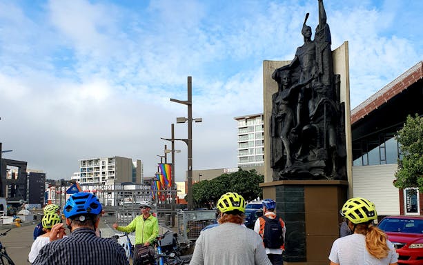 Group of cyclists listening to a guide near a statue in Wellington, New Zealand.