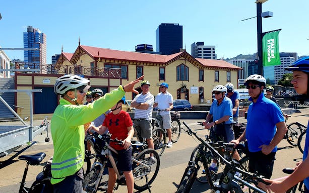Cyclists gather for a guided bike tour in Wellington, New Zealand, near historic buildings.