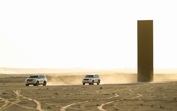 SUVs driving near Richard Serra sculpture in Zekreet Desert, Qatar.