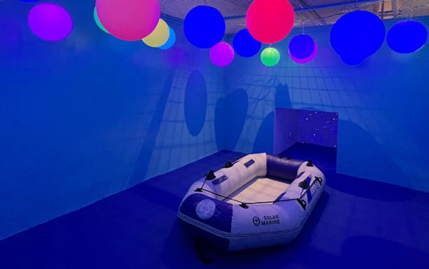 Inflatable boat in a blue room with colorful glowing spheres at Otah & Friends: Camp Stardust.