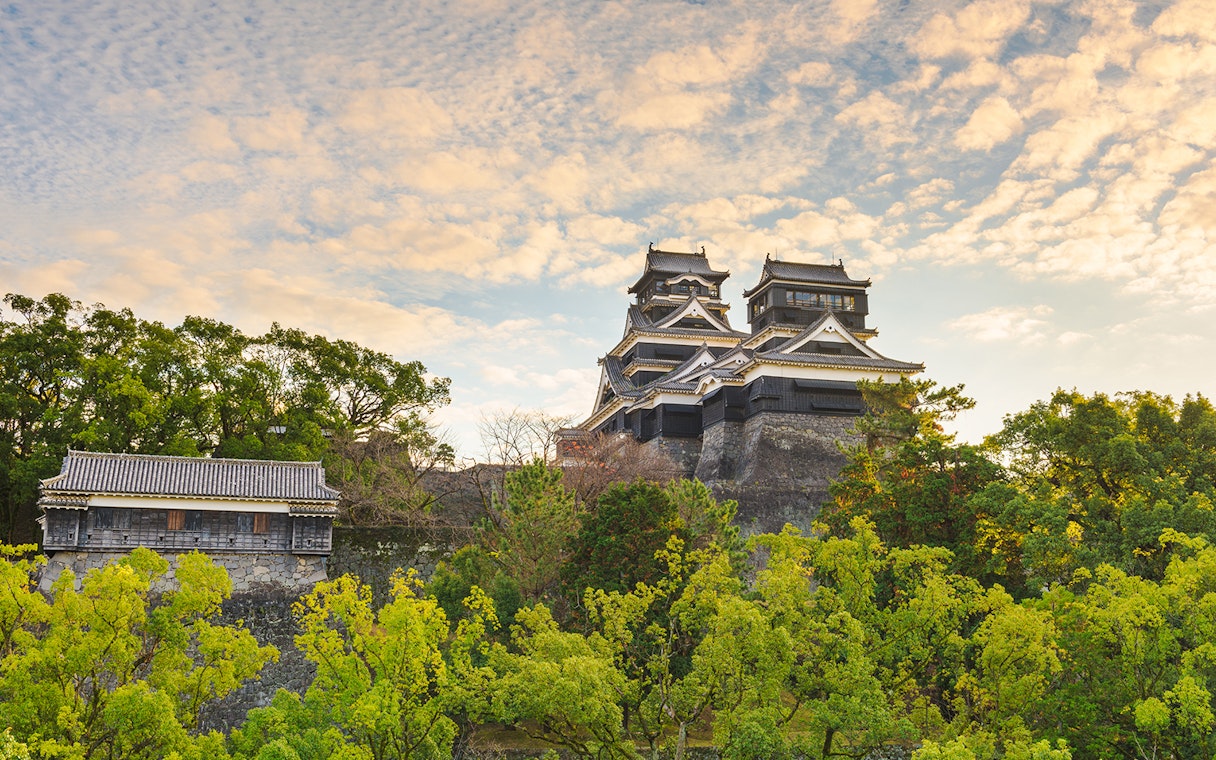 Kumamoto Castle surrounded by lush greenery under a cloudy sky in Southern Kyushu.