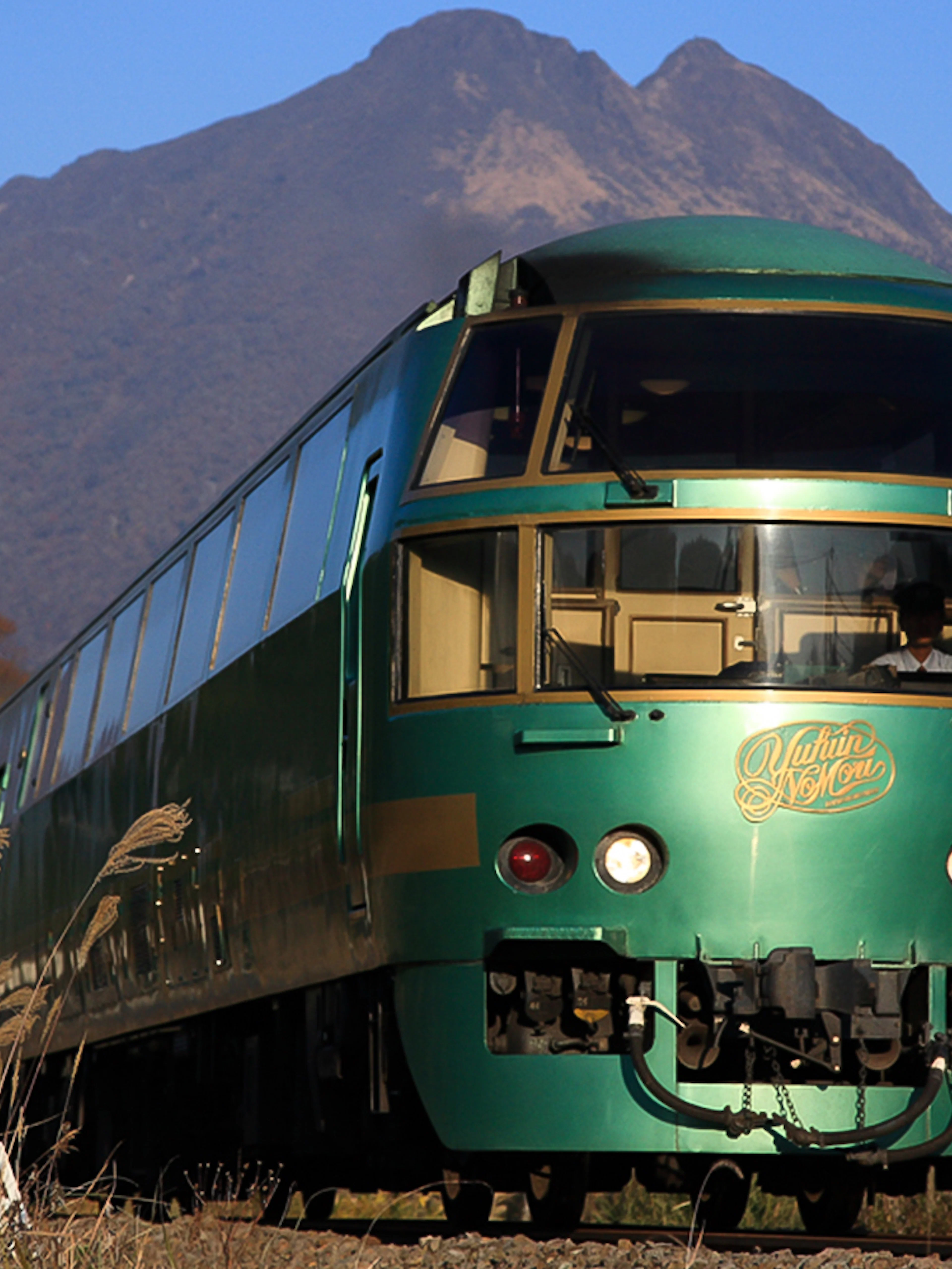 Green train on JR North Kyushu Rail Pass route with mountain backdrop.