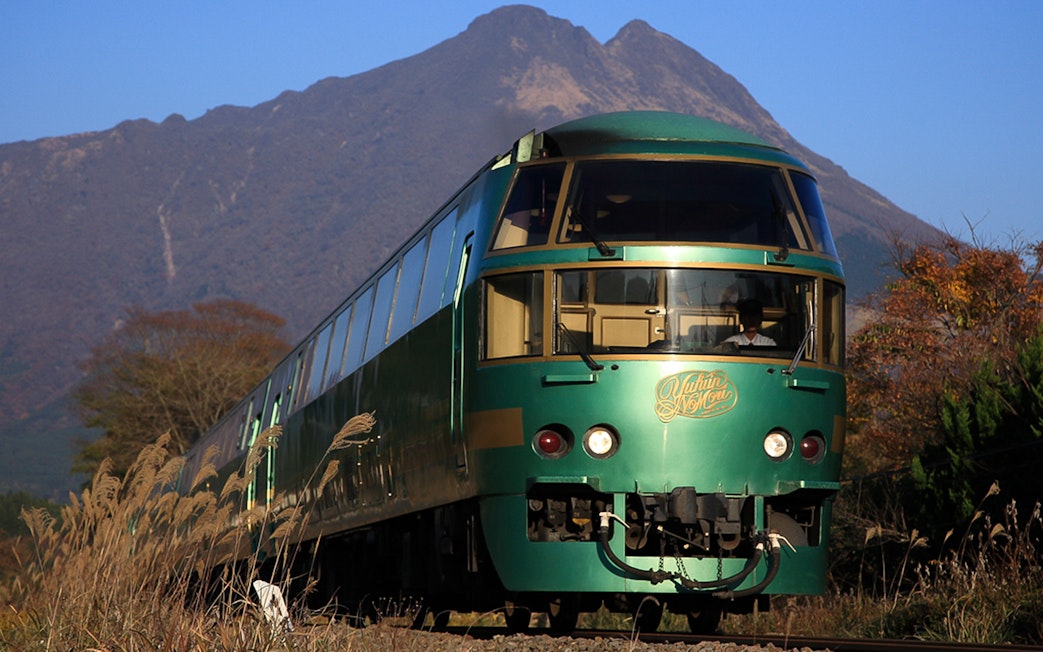 Green train on JR North Kyushu Rail Pass route with mountain backdrop.