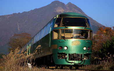 Green train on JR North Kyushu Rail Pass route with mountain backdrop.