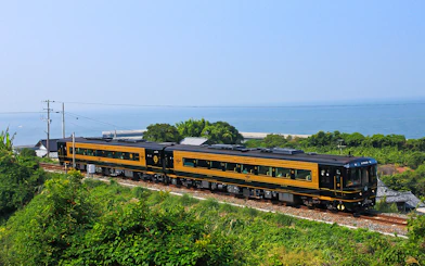 Train traveling along Kyushu coast with ocean view, JR North Kyushu Rail Pass.