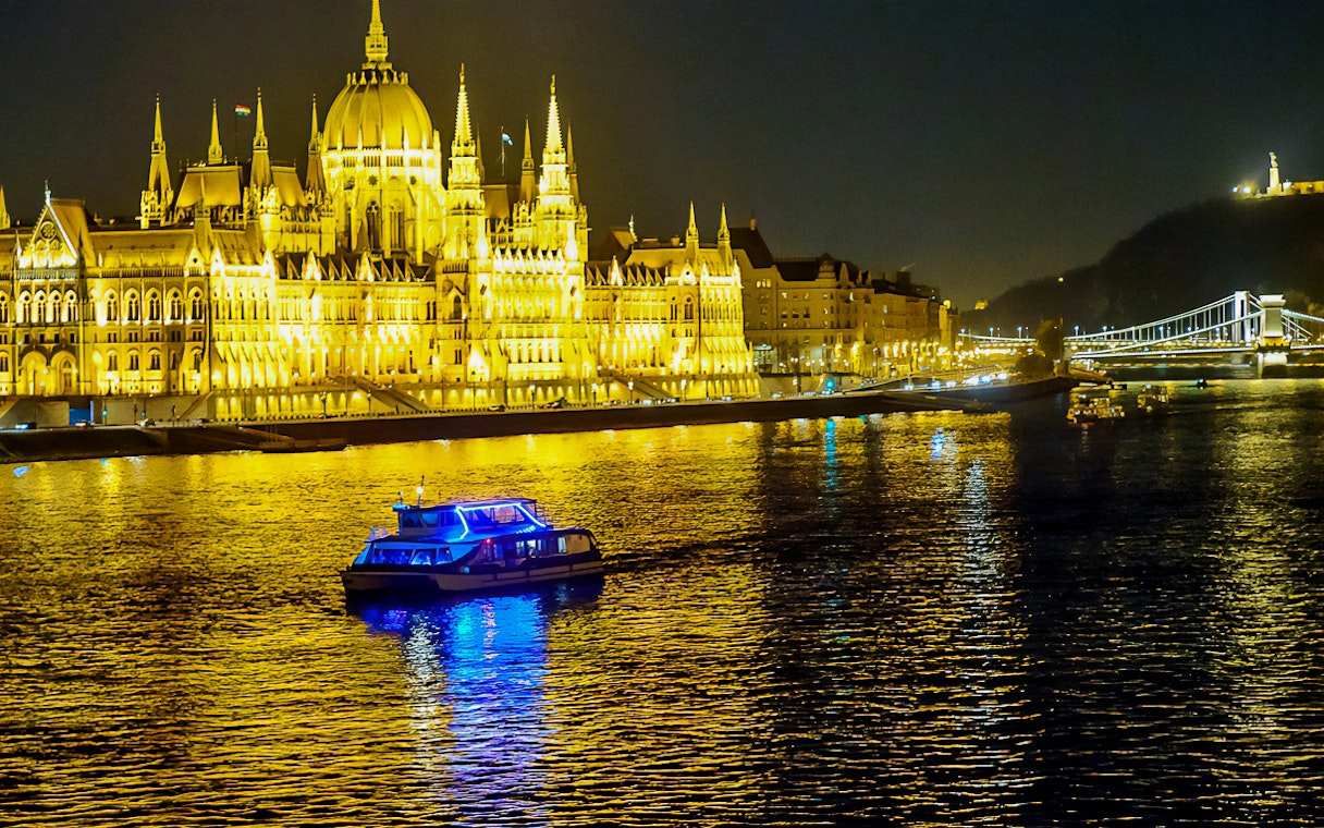Cruise boat on the Danube River in Budapest at night, near illuminated Parliament building.