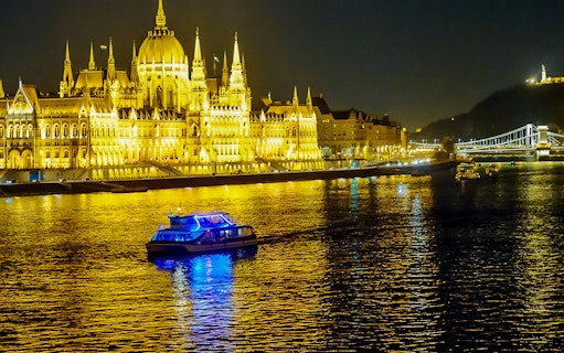 Cruise boat on the Danube River in Budapest at night, near illuminated Parliament building.