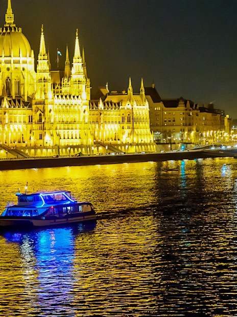 Cruise boat on the Danube River in Budapest at night, near illuminated Parliament building.