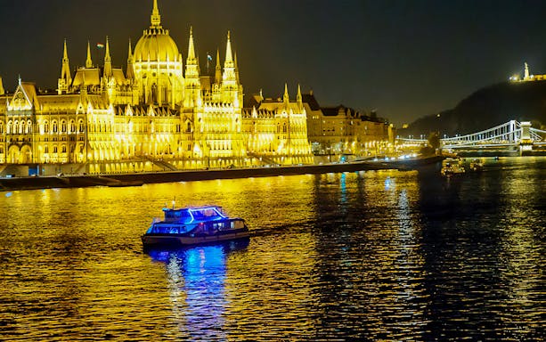 Cruise boat on the Danube River in Budapest at night, near illuminated Parliament building.