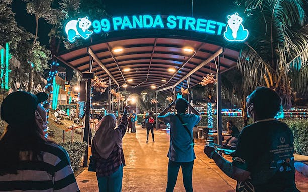 Visitors at night under the illuminated 99 Panda Street sign at 99 Wonderland Park.