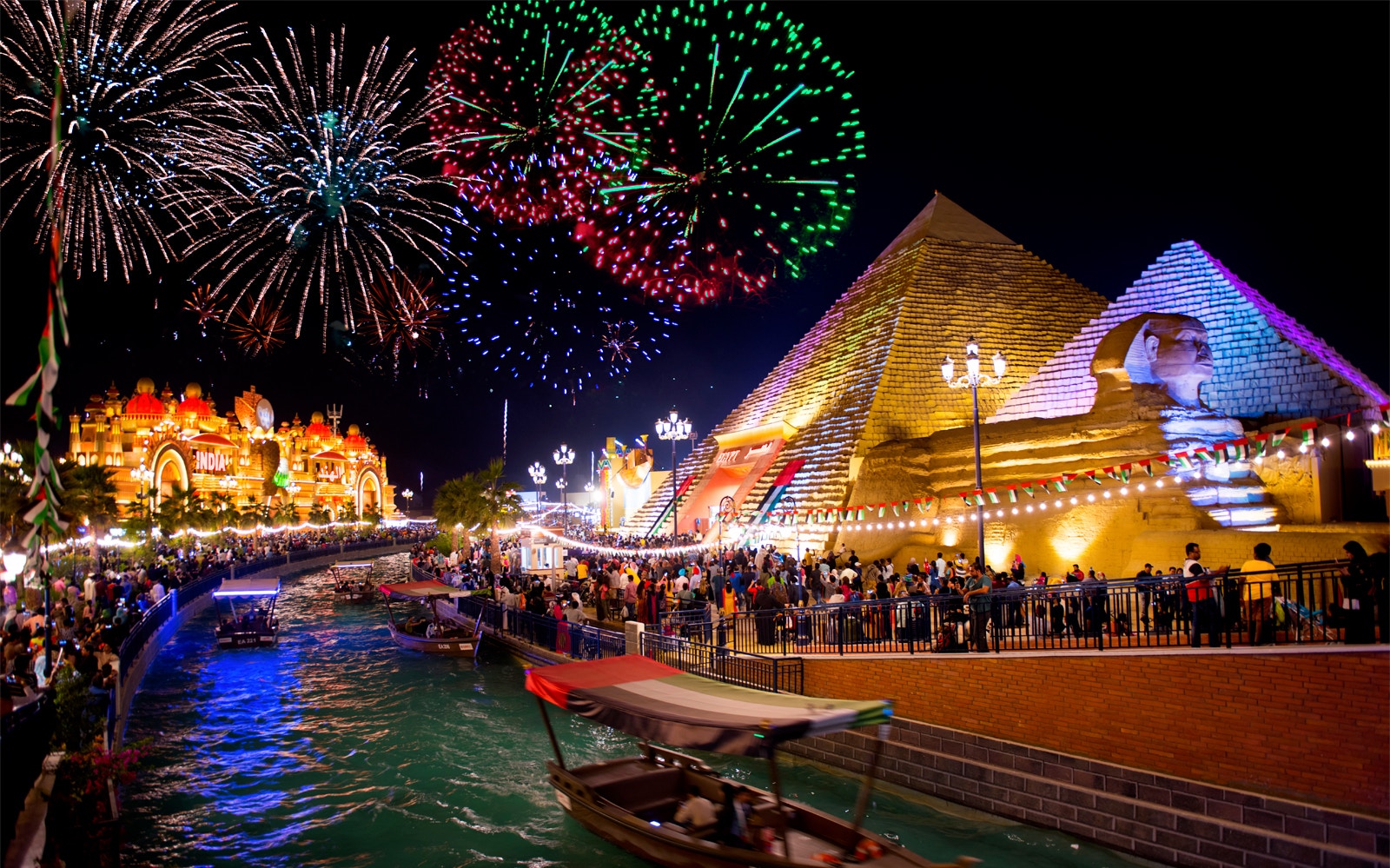 Fireworks over Dubai Global Village with illuminated pyramids and canal.