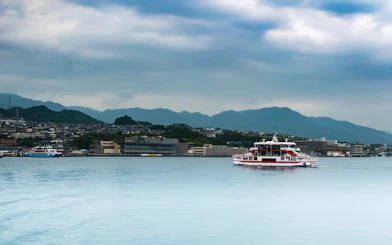 Ferry crossing Seto Inland Sea with Hiroshima cityscape and mountains in background.