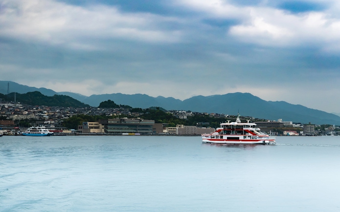 Ferry crossing Seto Inland Sea with Hiroshima cityscape and mountains in background.