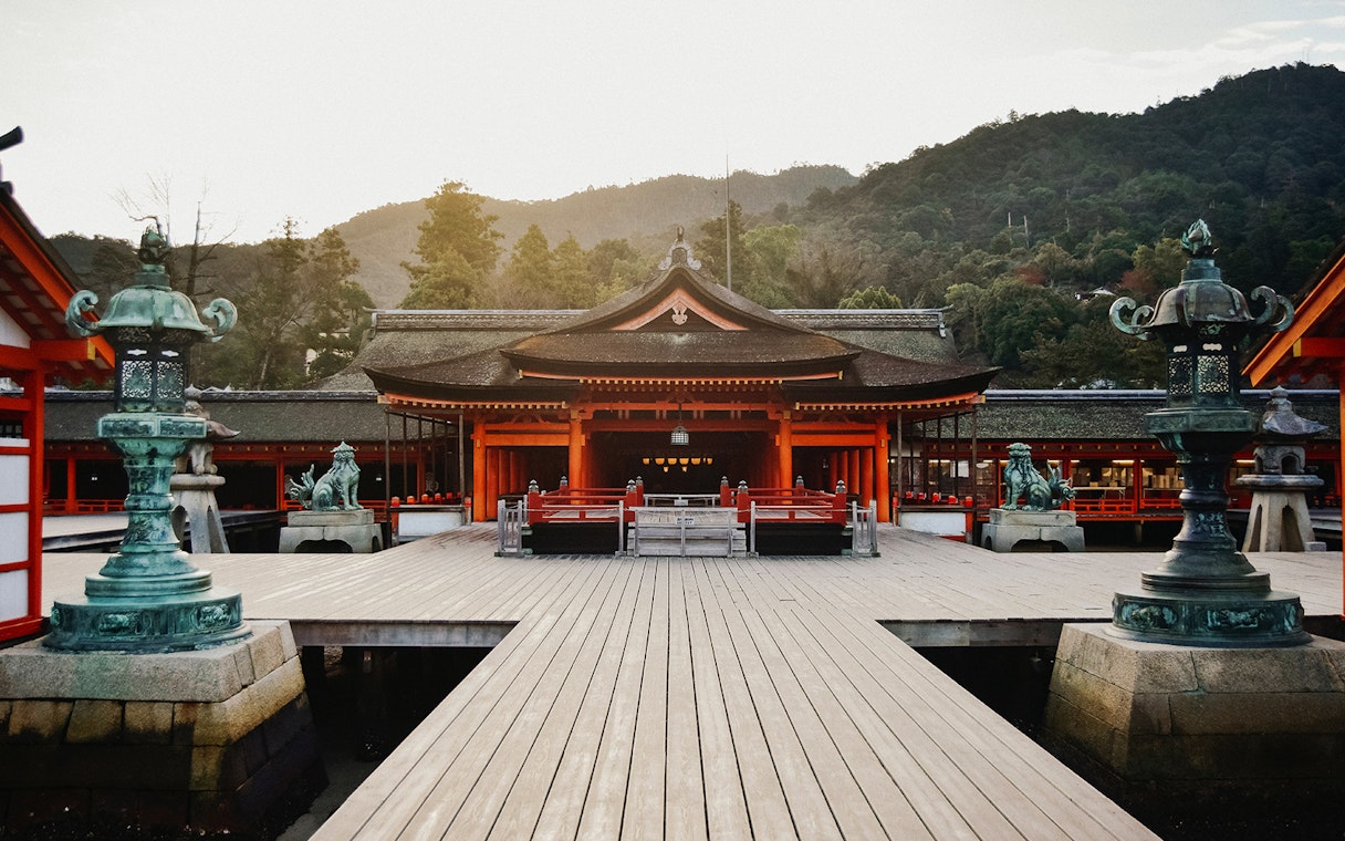 Itsukushima Shrine in Hiroshima, Japan, with traditional architecture and surrounding mountains.