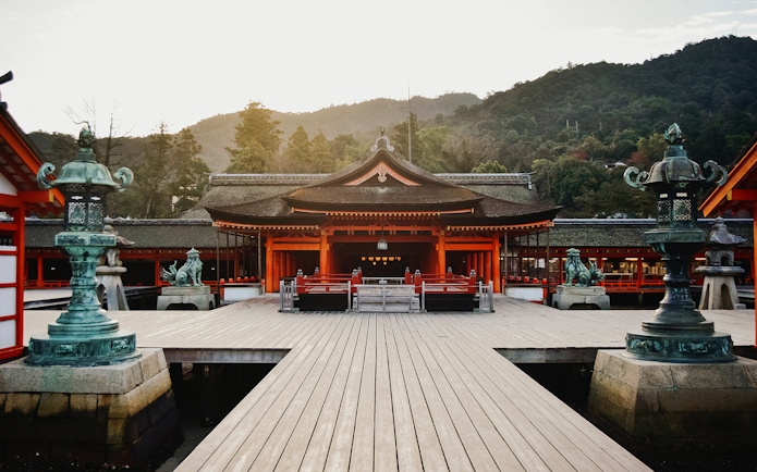 Itsukushima Shrine in Hiroshima, Japan, with traditional architecture and surrounding mountains.
