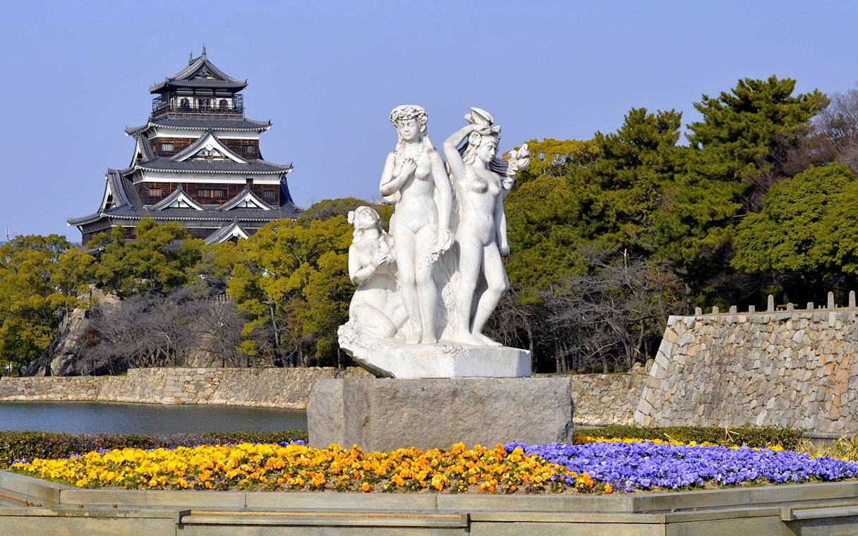 Hiroshima Castle with a statue and colorful flowers in the foreground, Japan.