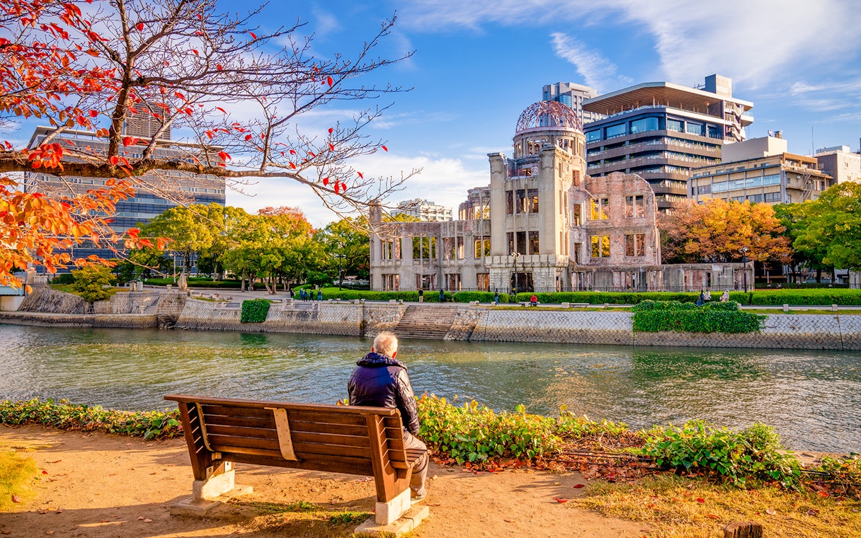 Hiroshima Peace Memorial with autumn foliage, viewed from across the river.