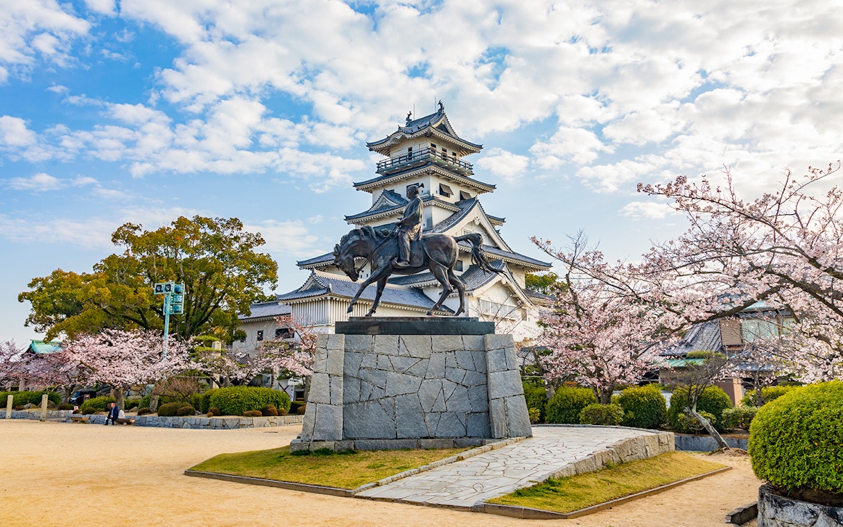 Matsuyama Castle with cherry blossoms and equestrian statue, Setouchi, Japan.