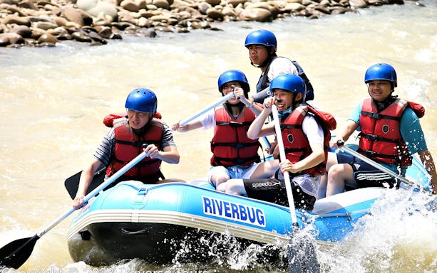 Group enjoying white water rafting on a river in Sabah, wearing helmets and life vests.