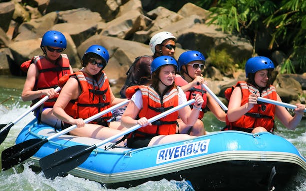 White water rafting group navigating rapids in Sabah, wearing helmets and life vests.