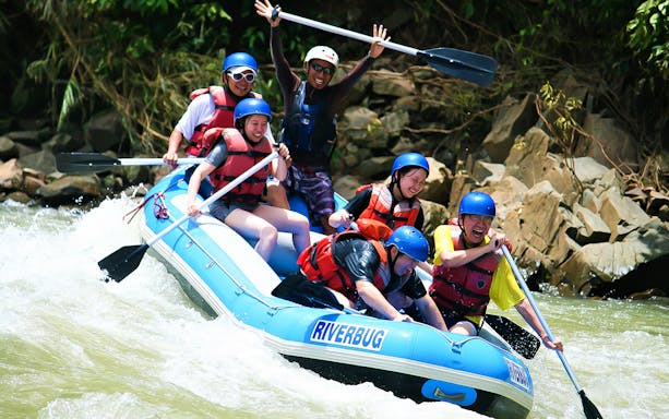 White water rafting group navigating rapids in Sabah, wearing helmets and life jackets.
