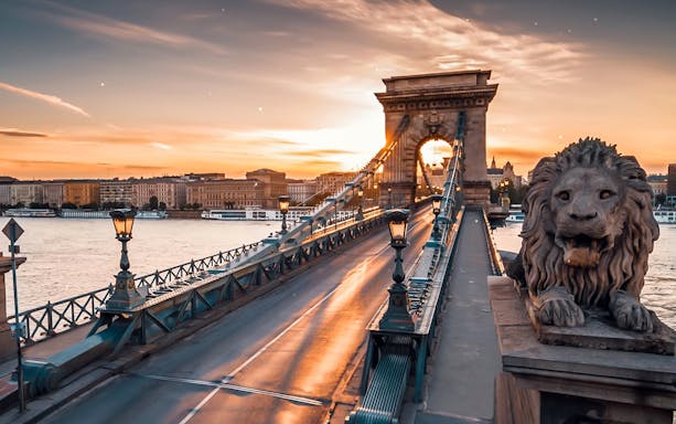 Chain Bridge in Budapest at sunset with lion statue and cityscape in the background.