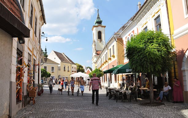Street scene in Szentendre with people walking and a church tower in the background.