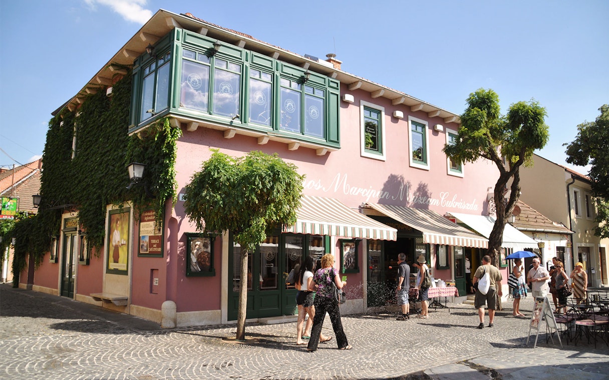 Szentendre street with tourists outside a pink building covered in ivy, Hungary.