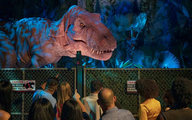 Visitors observing a large dinosaur model at Jurassic World: The Exhibition in London.