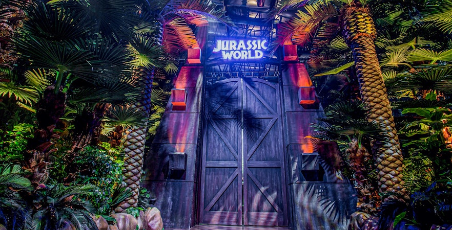 Entrance gate to Jurassic World: The Exhibition surrounded by lush greenery.