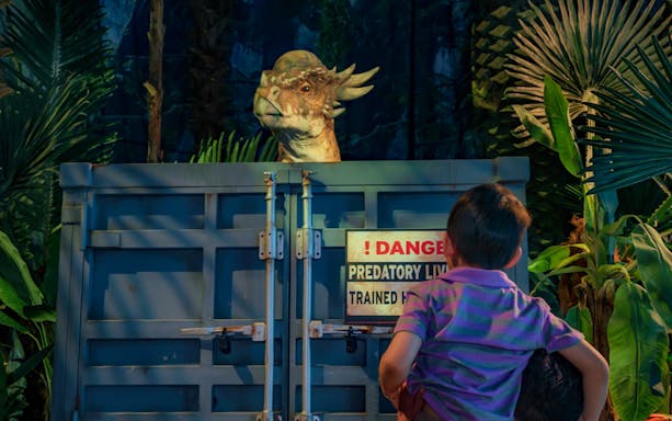 Child observing dinosaur behind gate at Jurassic World: The Exhibition, London.