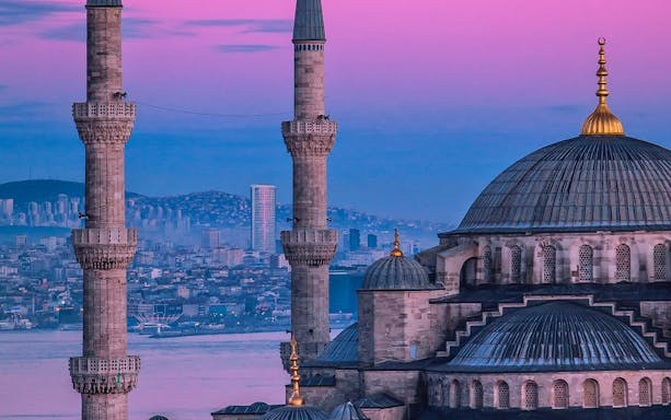 Blue Mosque domes and minarets at sunset, Istanbul skyline in background.