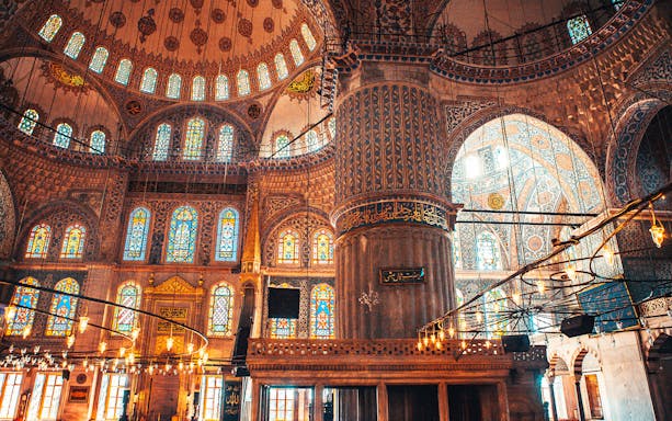 Interior of the Blue Mosque with ornate stained glass windows and intricate tilework.