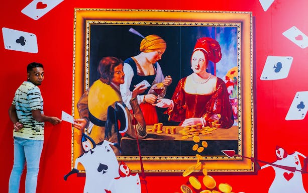 Man interacting with 3D art at Trick Eye Museum, featuring a classic painting and playing cards.