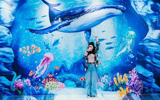 Visitor posing with underwater mural at Trick Eye Museum, featuring a whale and colorful sea life.