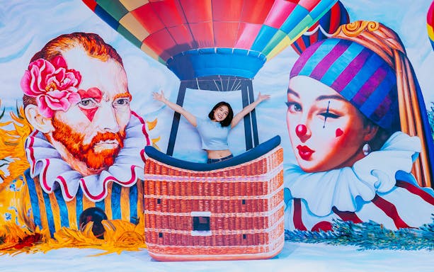 Person posing in a hot air balloon basket at Trick Eye Museum with vibrant murals.