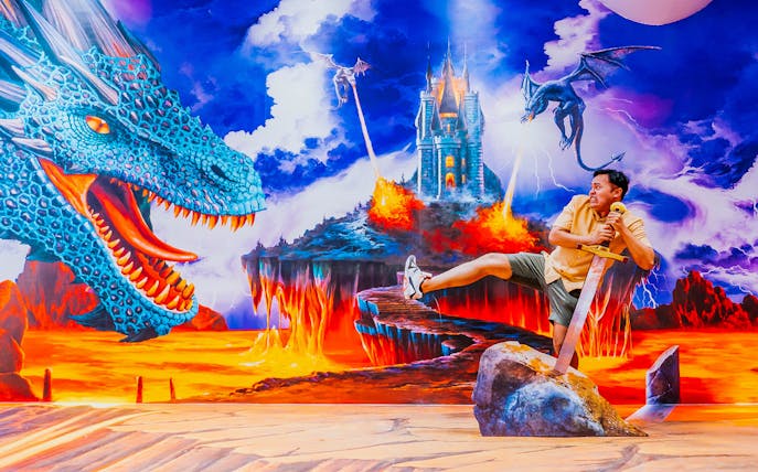 Man posing with sword in fantasy dragon scene at Trick Eye Museum, Headrock VR 'Play 2'.
