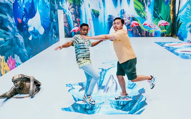 Visitors interacting with 3D art at Trick Eye Museum, featuring dolphins and a waterfall.