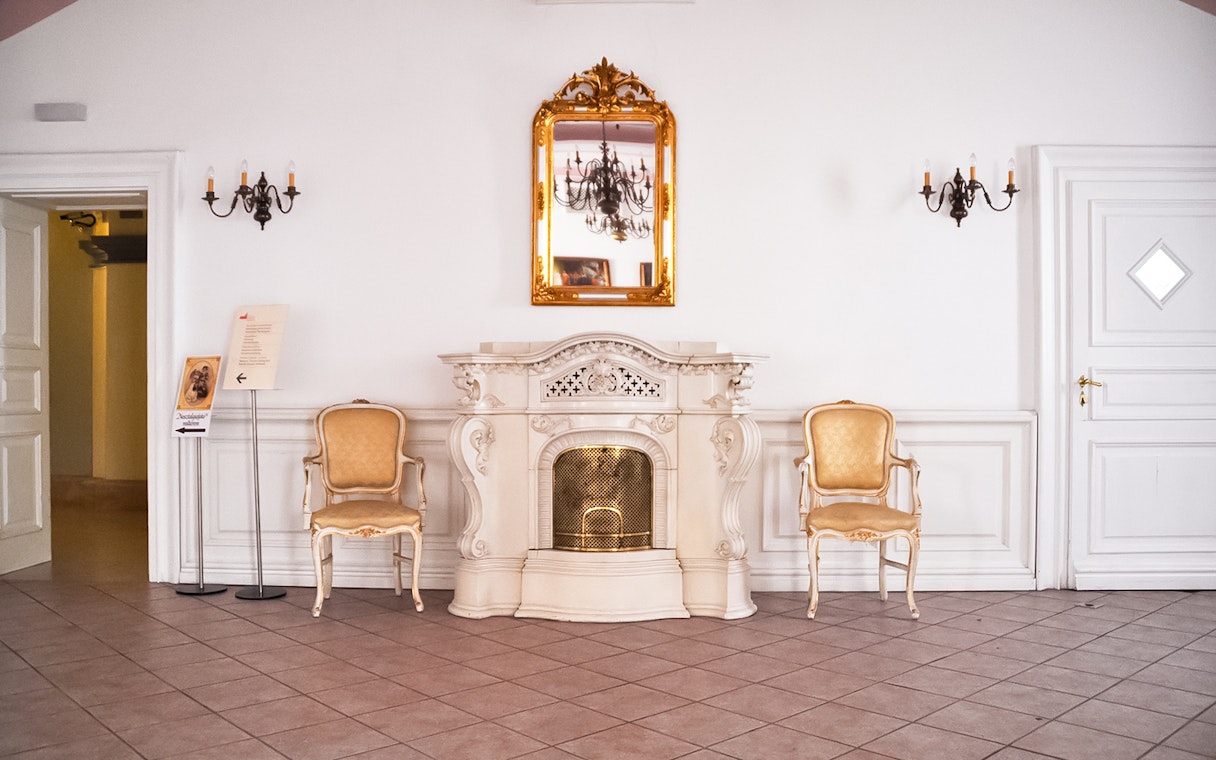 Elegant interior of Gödöllő Palace with ornate fireplace and chairs, Budapest tour.