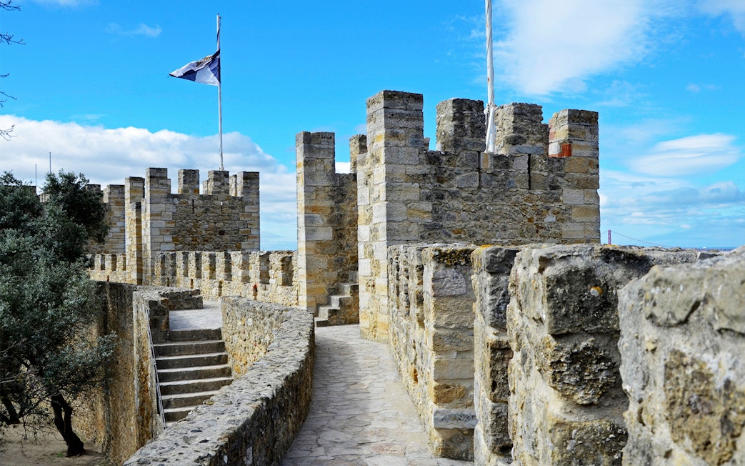 Towers and stone walls of St. George’s Castle in Lisbon under a blue sky.