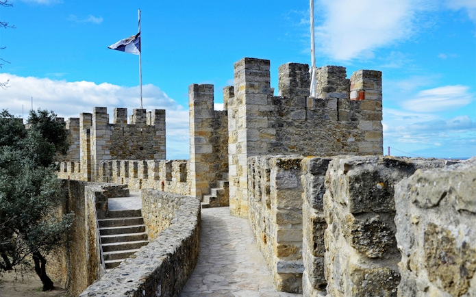 Towers and stone walls of St. George’s Castle in Lisbon under a blue sky.