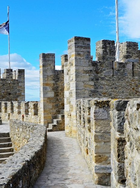 Towers and stone walls of St. George’s Castle in Lisbon under a blue sky.