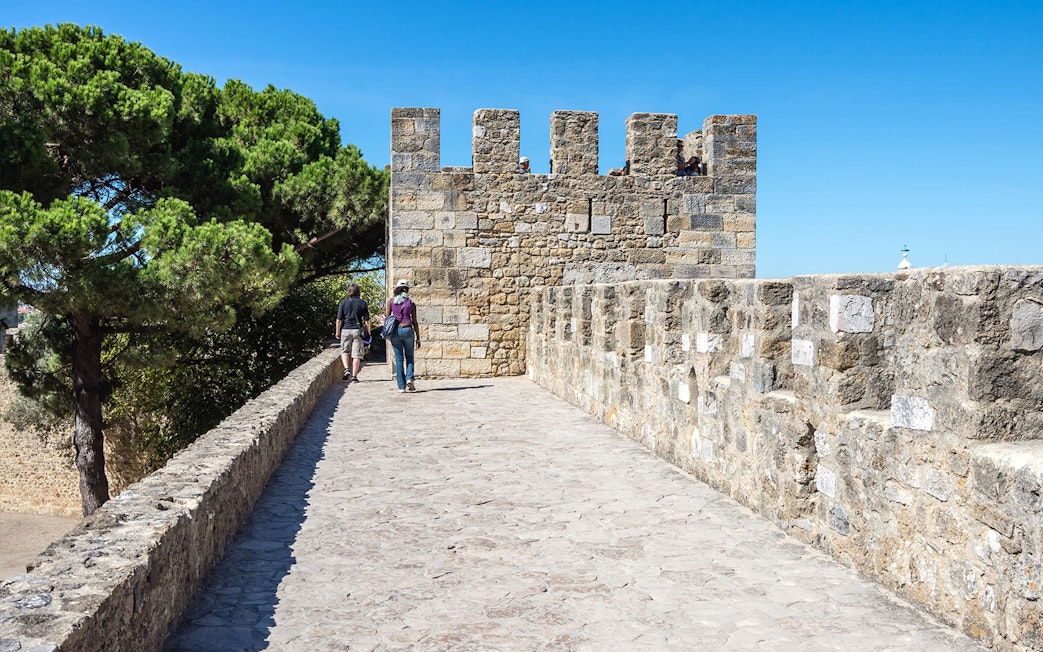 Tourists walking along the stone walls of St. George Castle in Lisbon.