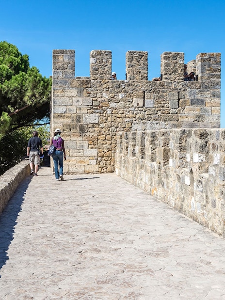 Tourists walking along the stone walls of St. George Castle in Lisbon.