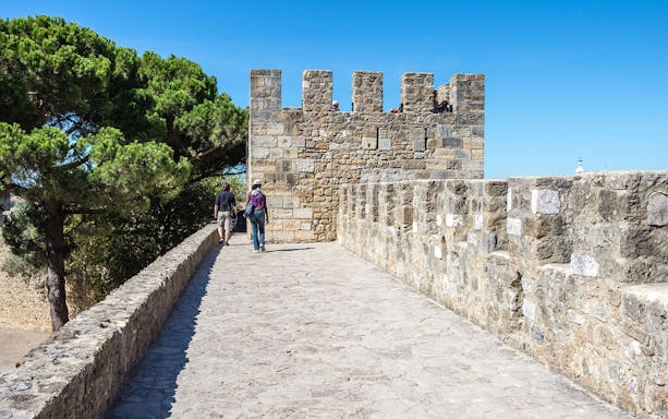 Tourists walking along the stone walls of St. George Castle in Lisbon.