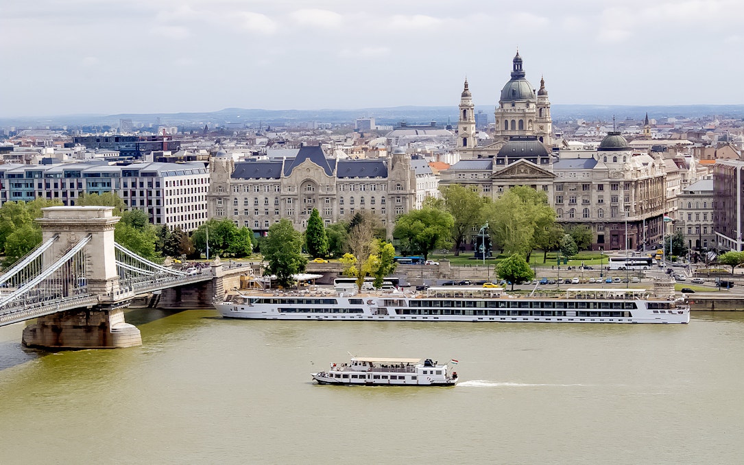 Danube River cruise boat passing by Budapest's Chain Bridge and historic buildings.